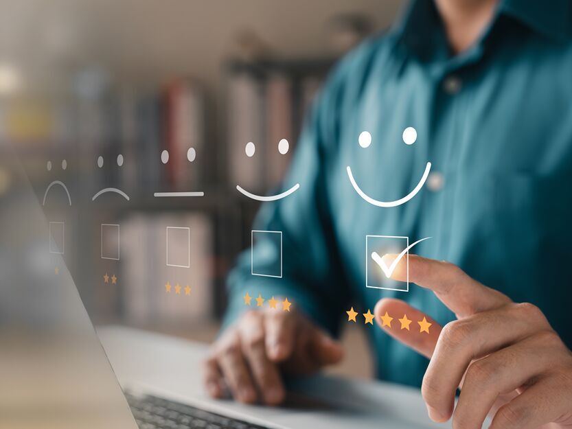 Symbolbild für Kundenzufriedenheit: Hand am Laptop gibt digitale Fünf-Sterne-Bewertung mit Smiley ab